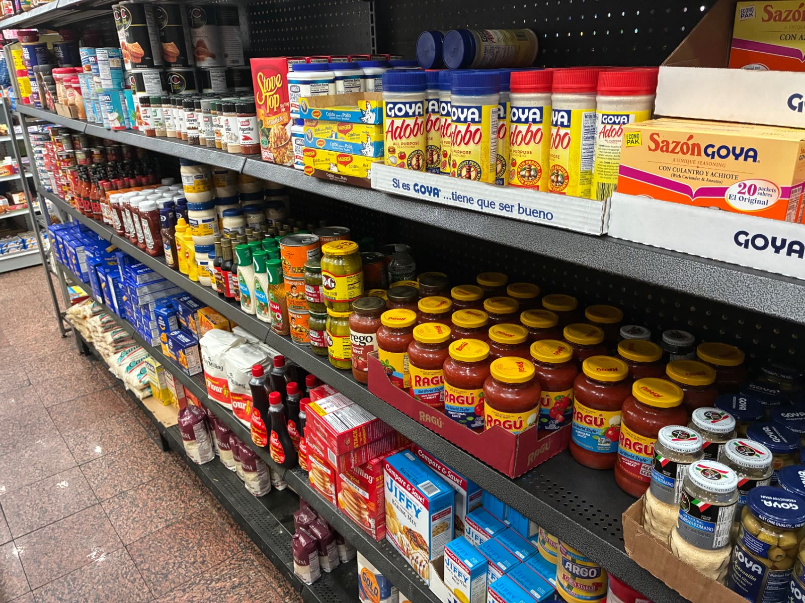 Grocery shelves stocked with Goya seasonings, pasta sauce, spices and baking staples inside The Famous Deli